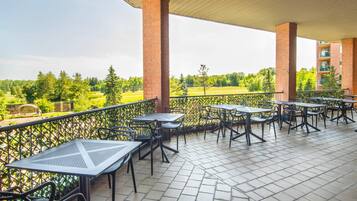 Un patio techado al aire libre con mesas y sillas, pilares de ladrillo y vistas a un paisaje verde.