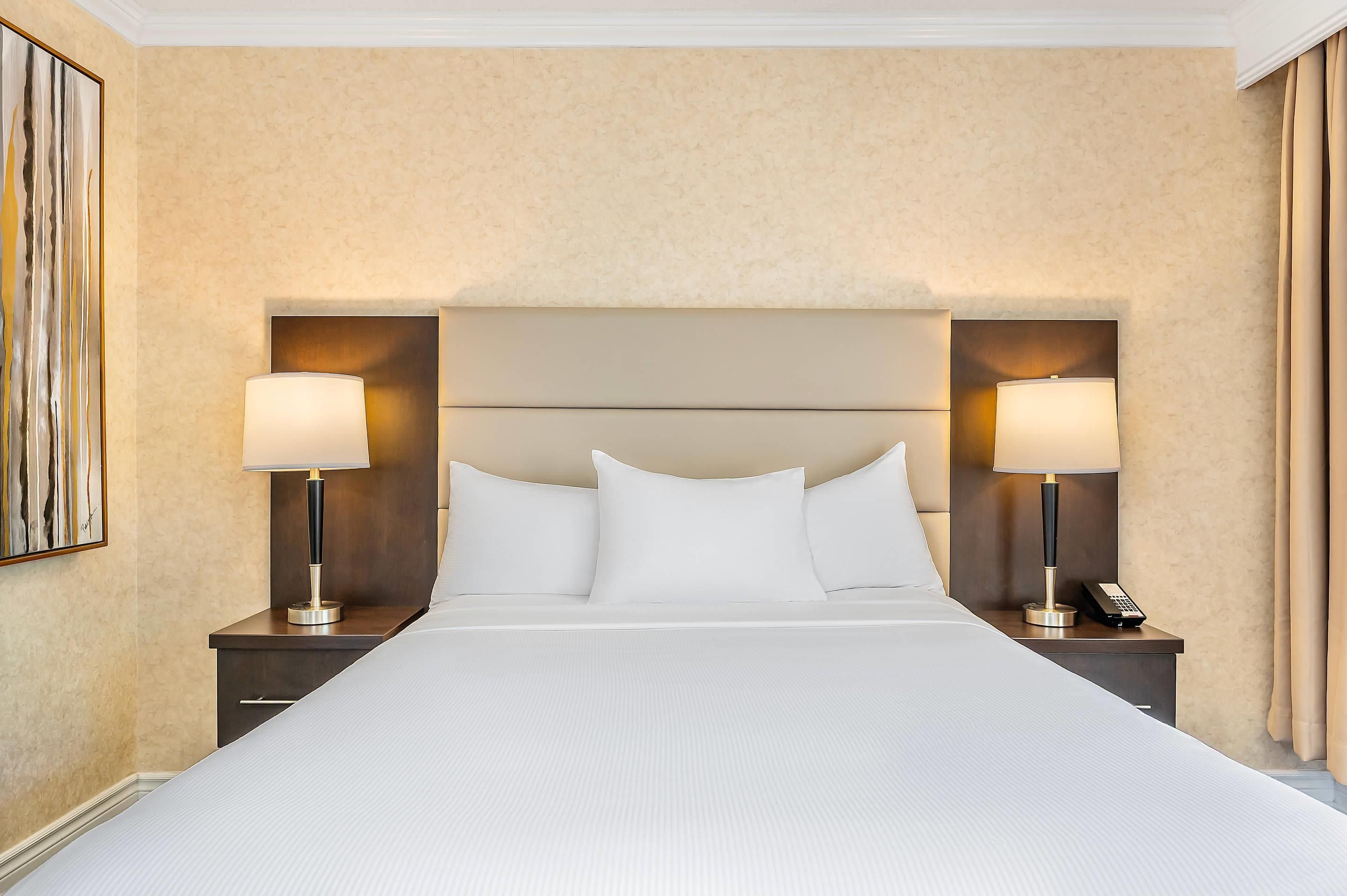 A hotel room with a large bed, two bedside tables with lamps, a headboard, and a painting on the wall.