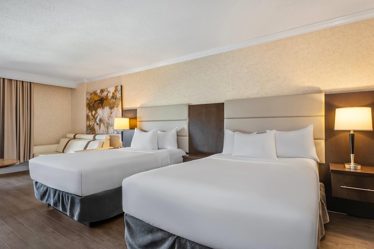 Habitación de hotel con dos camas, un sofá, un cuadro en la pared y dos lámparas de noche.