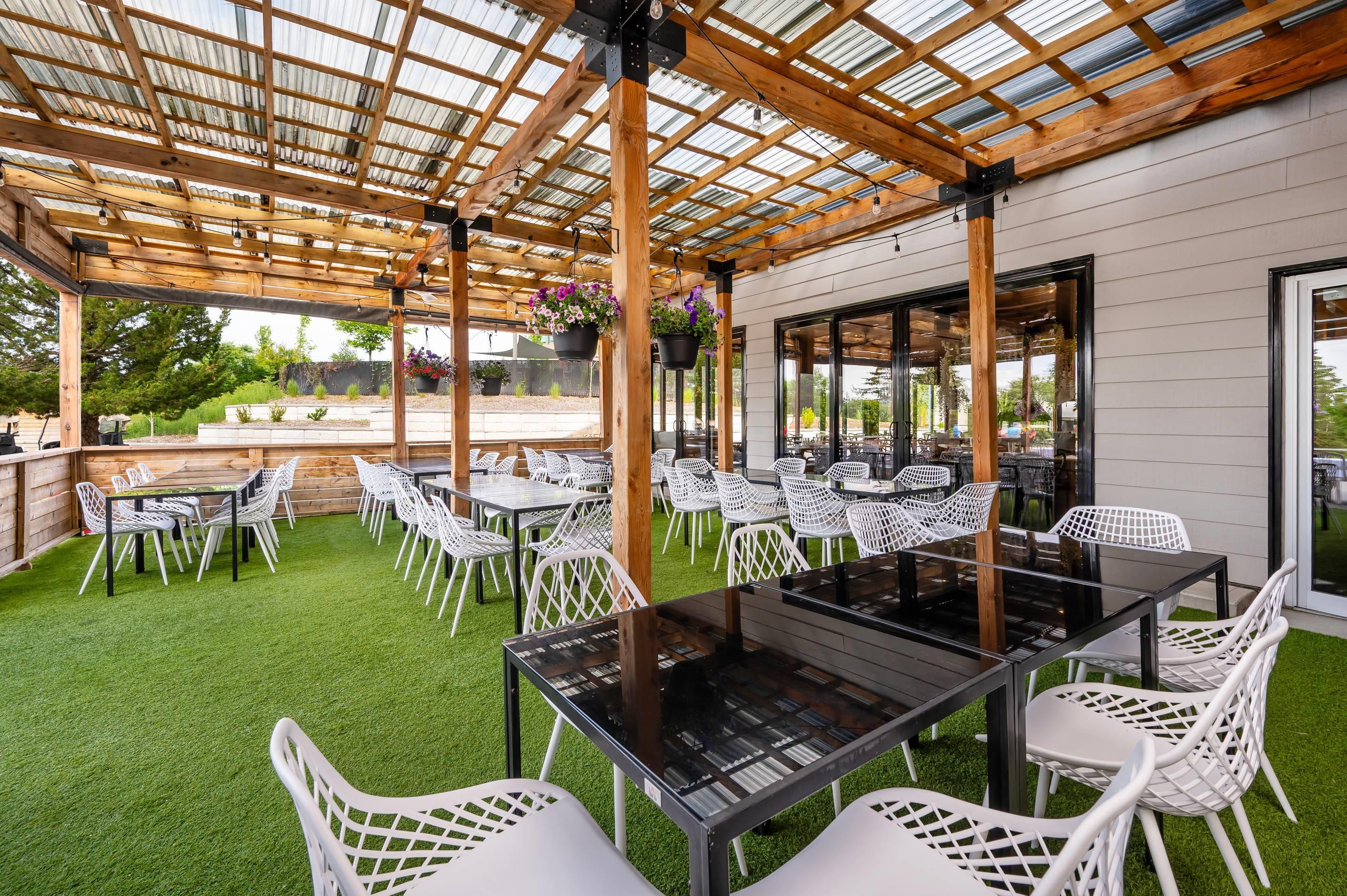 En udendørs terrasse med borde og stole, en pergola og udsigt til haven.
