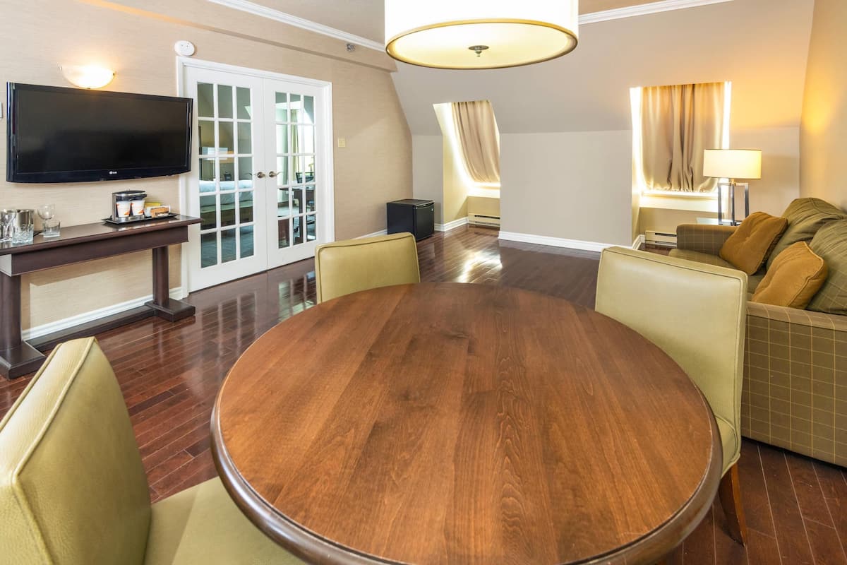 Une chambre d’hôtel comprenant une table de salle à manger ronde en bois, un canapé, un téléviseur et une porte donnant sur un balcon.