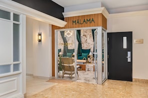 L’entrée d’un hôtel, avec une enseigne indiquant « MALAMA PARK KOEMA » et une porte portant la mention « 101-107 ».
