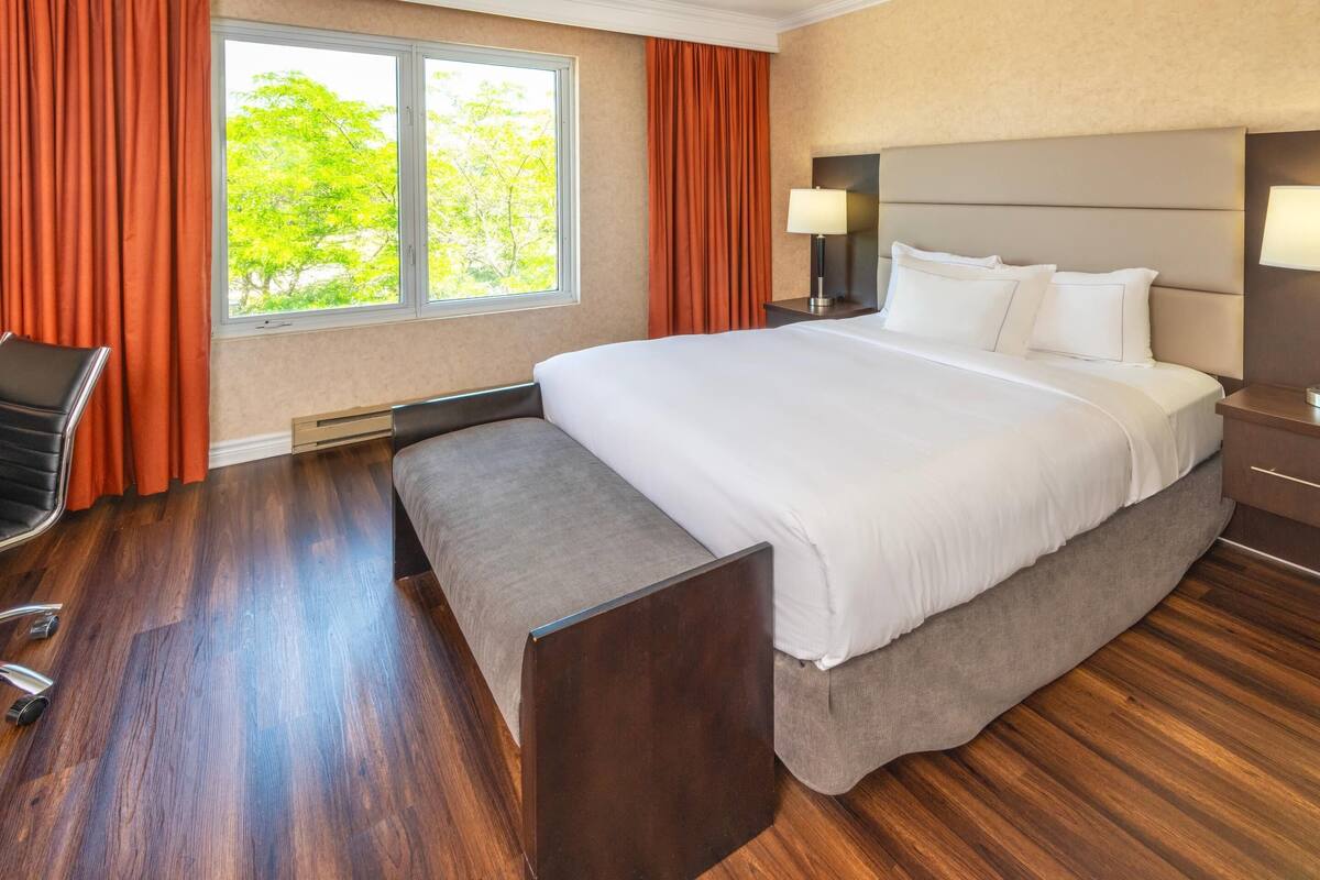 Une chambre d’hôtel avec un grand lit, un bureau, une chaise et une fenêtre avec des rideaux.