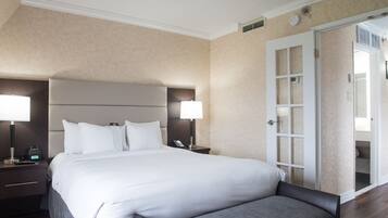 Une chambre d’hôtel avec un grand lit, deux tables de chevet avec des lampes, une tête de lit et une porte donnant sur une salle de bain.