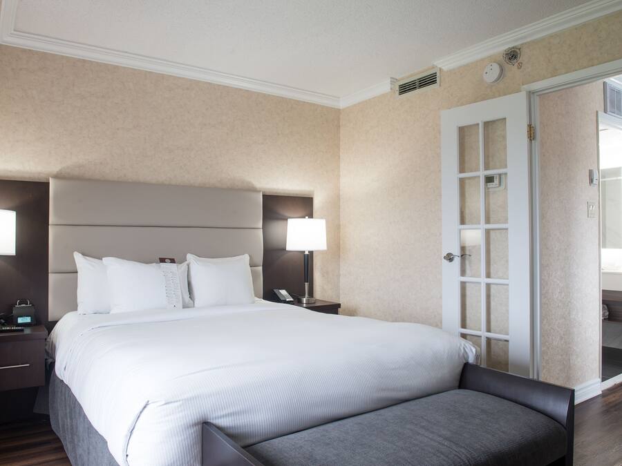 Une chambre d’hôtel avec un grand lit, deux tables de chevet avec des lampes, une tête de lit et une porte donnant sur une salle de bain.