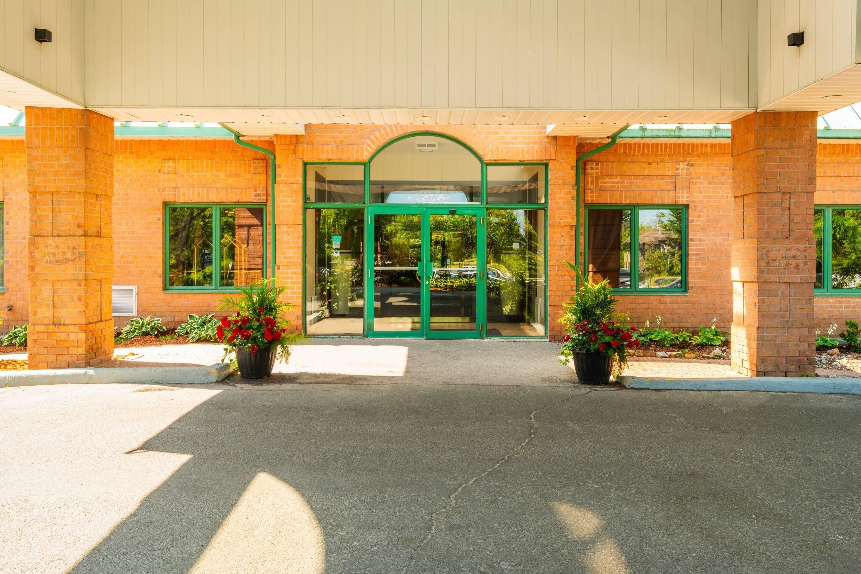 A building entrance with a green door, brick walls, and potted plants.