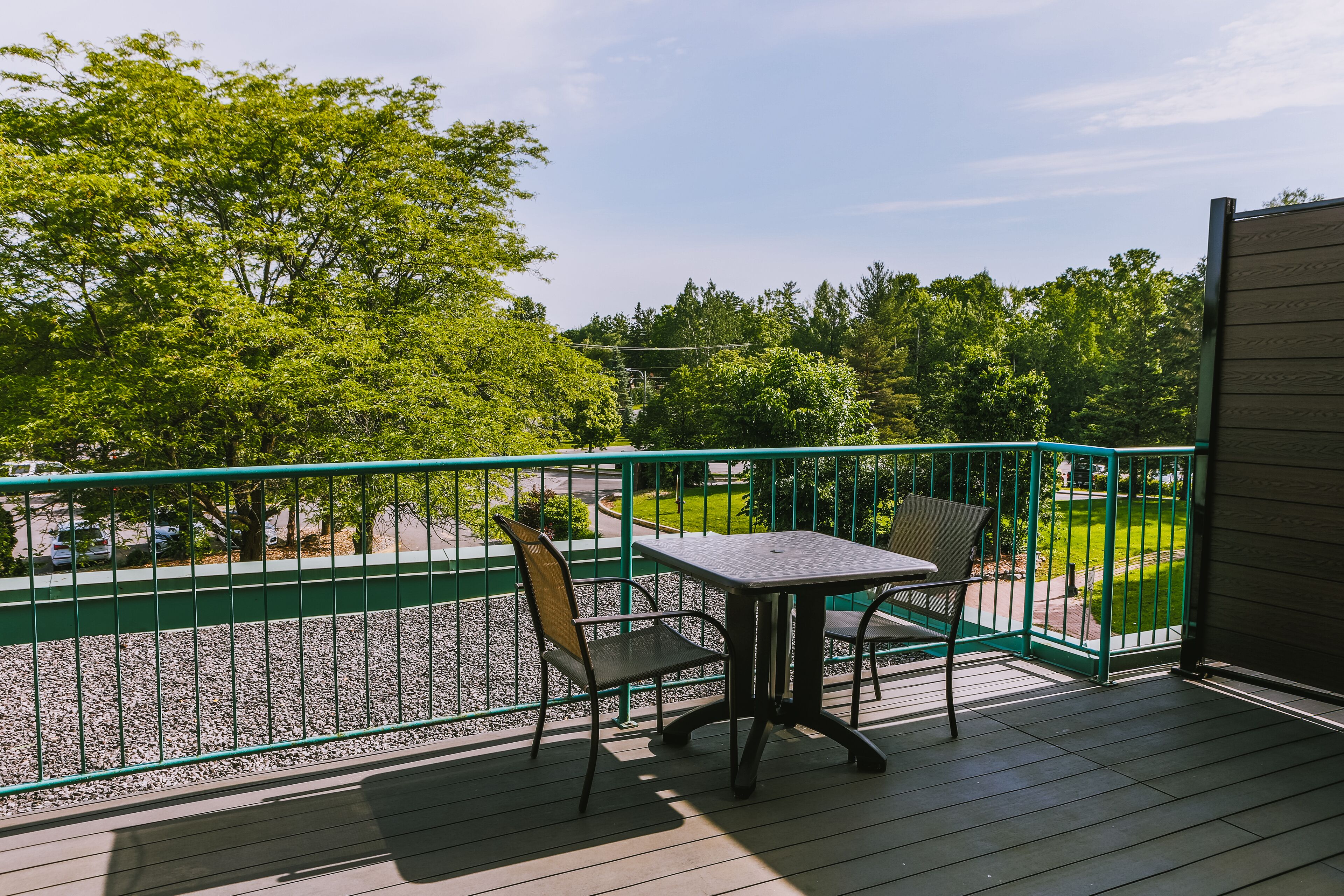 Un balcon avec une table et deux chaises, donnant sur un parc verdoyant et des arbres.