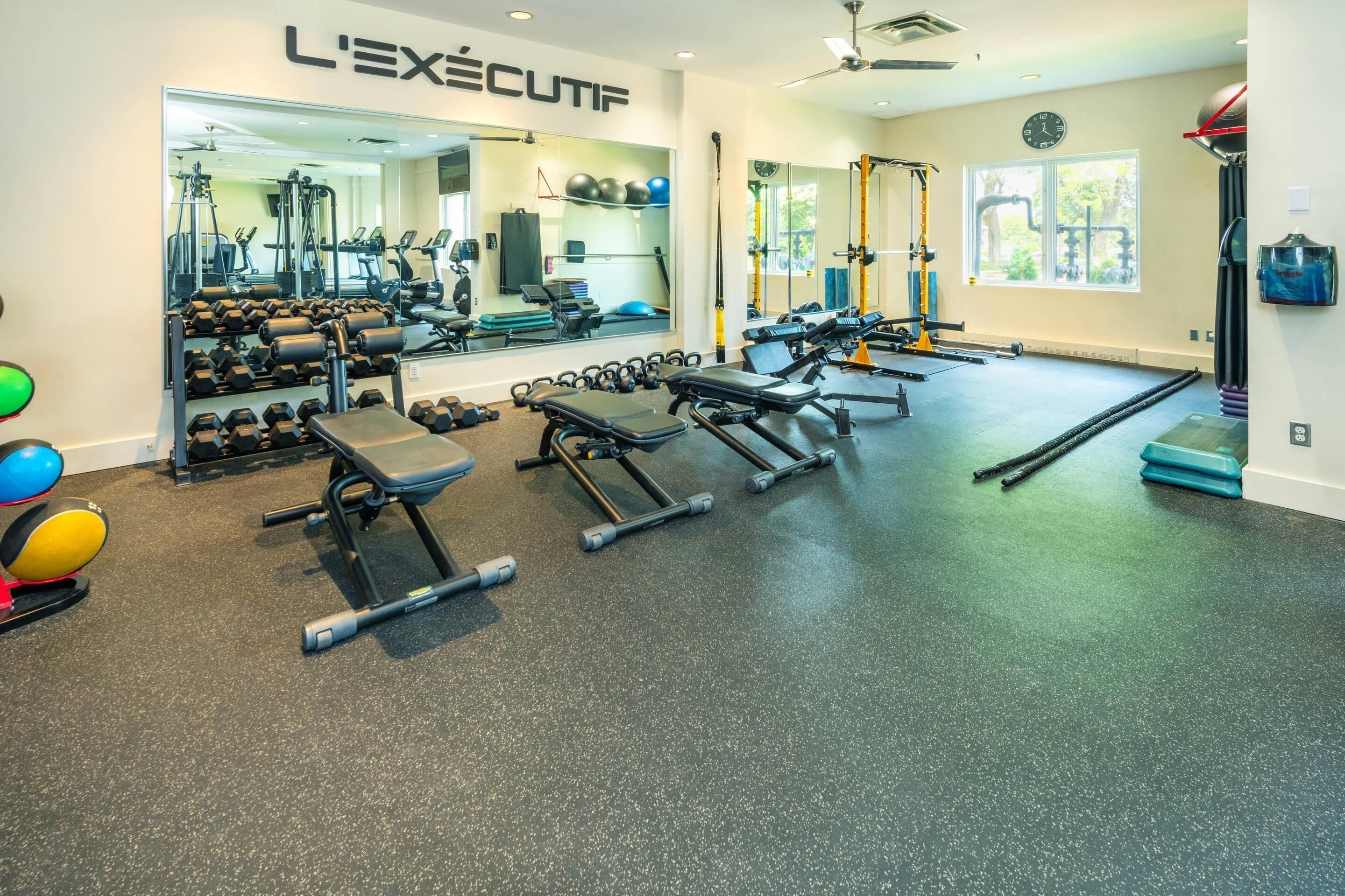 A gym with exercise equipment, a mirror, and a clock on the wall.