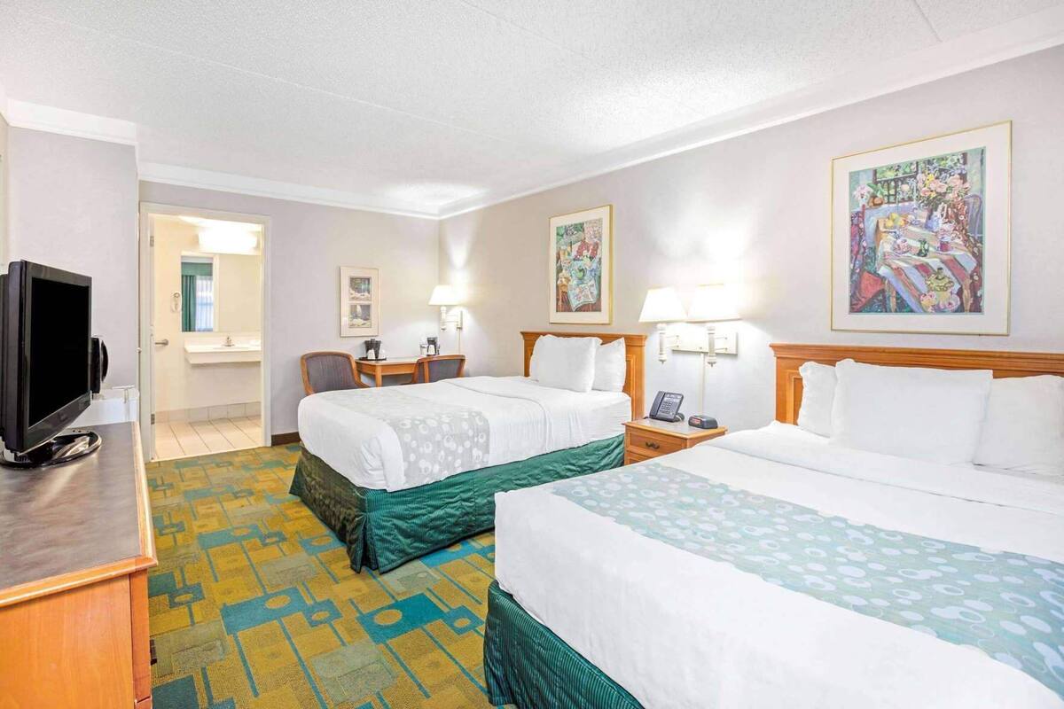A hotel room with two beds, a desk with a TV, a bathroom, and artwork on the walls.