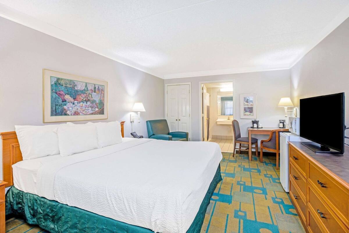 A hotel room with a large bed, a desk with a chair, a television, and a painting on the wall.