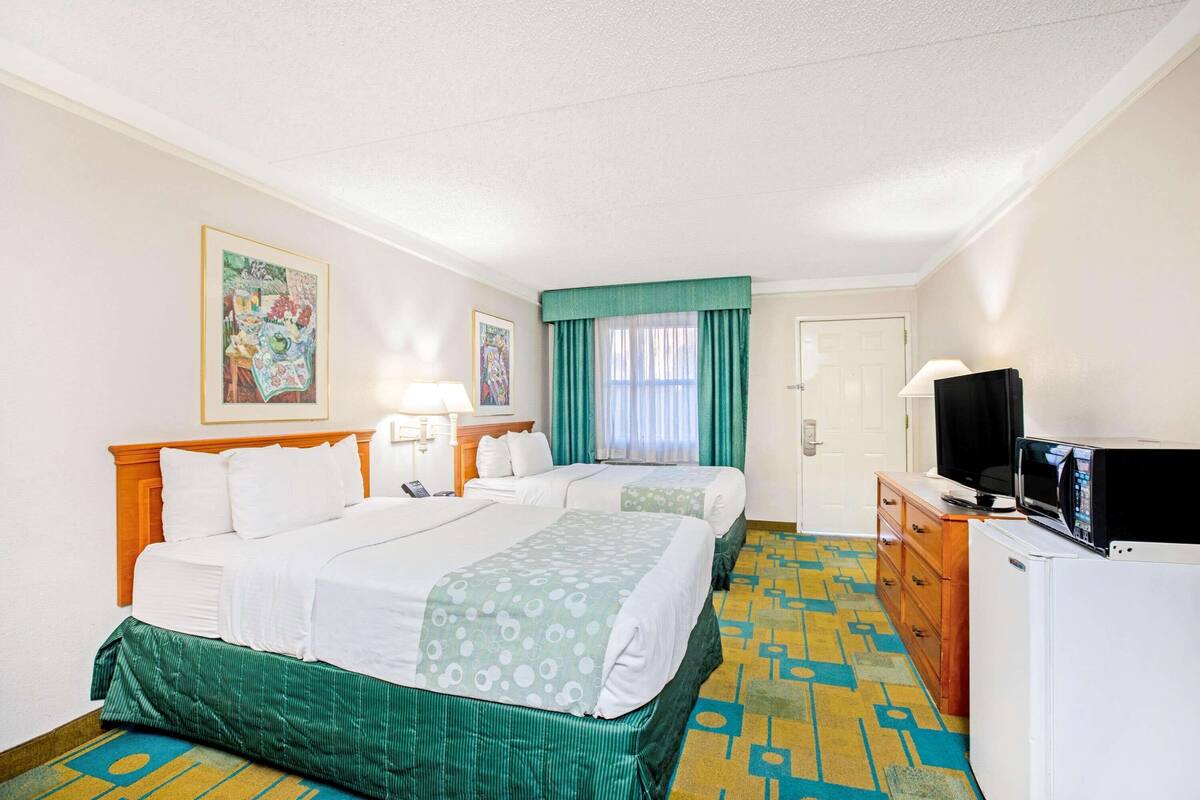 A hotel room with two beds, a television, a refrigerator, and a patterned carpet.