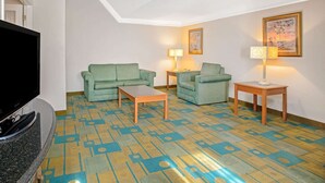 Una sala de estar con televisor de pantalla plana, dos sofás verdes, una mesa de centro de madera y una alfombra estampada.