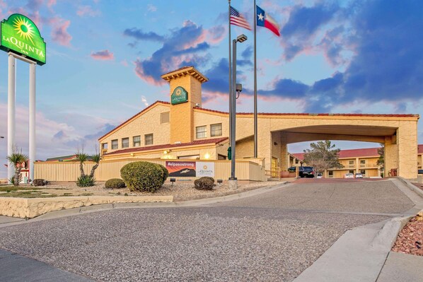 Un hotel La Quinta Inn con un amplio toldo de entrada, un letrero llamativo y una bandera estadounidense.