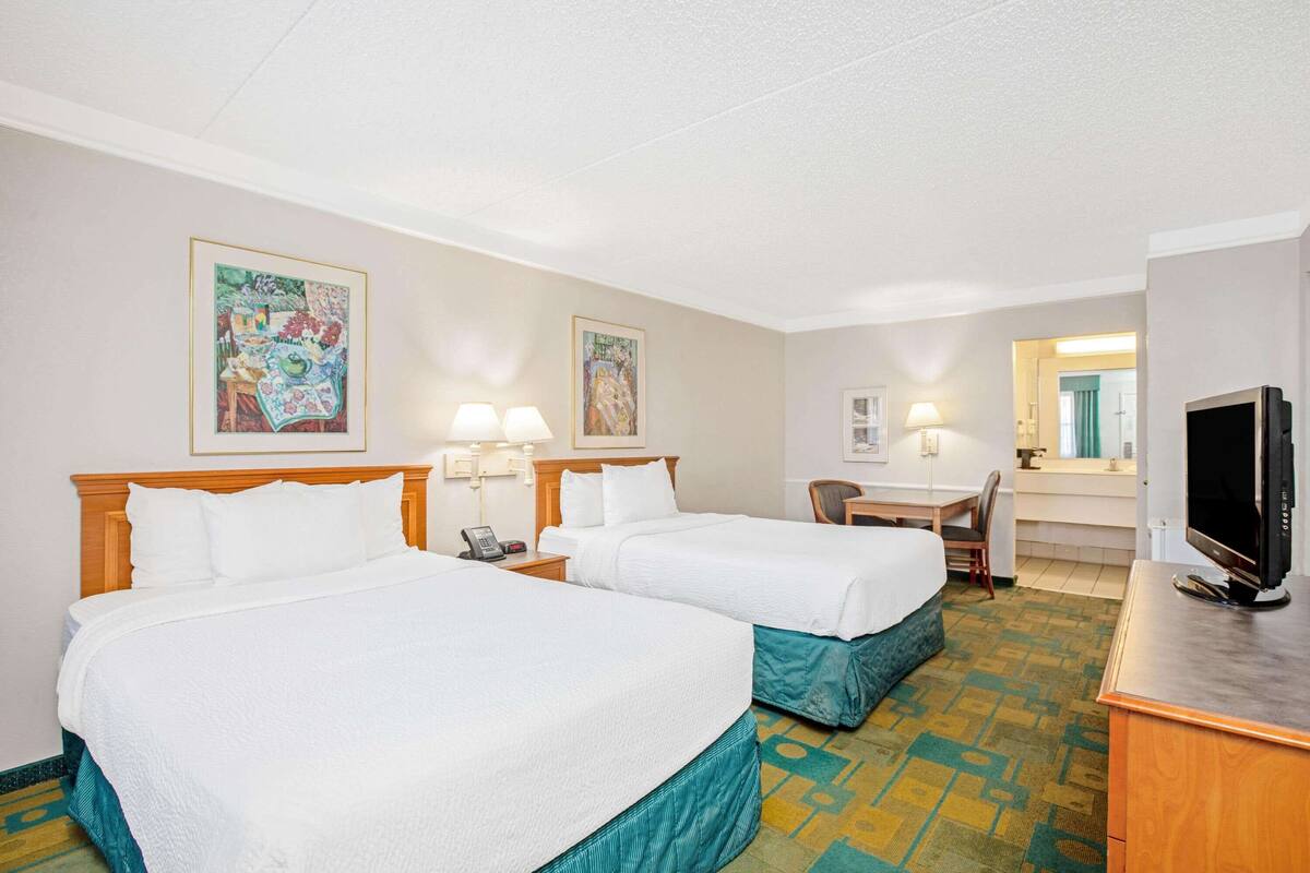 A hotel room with two beds, a desk, a television, and artwork on the walls.