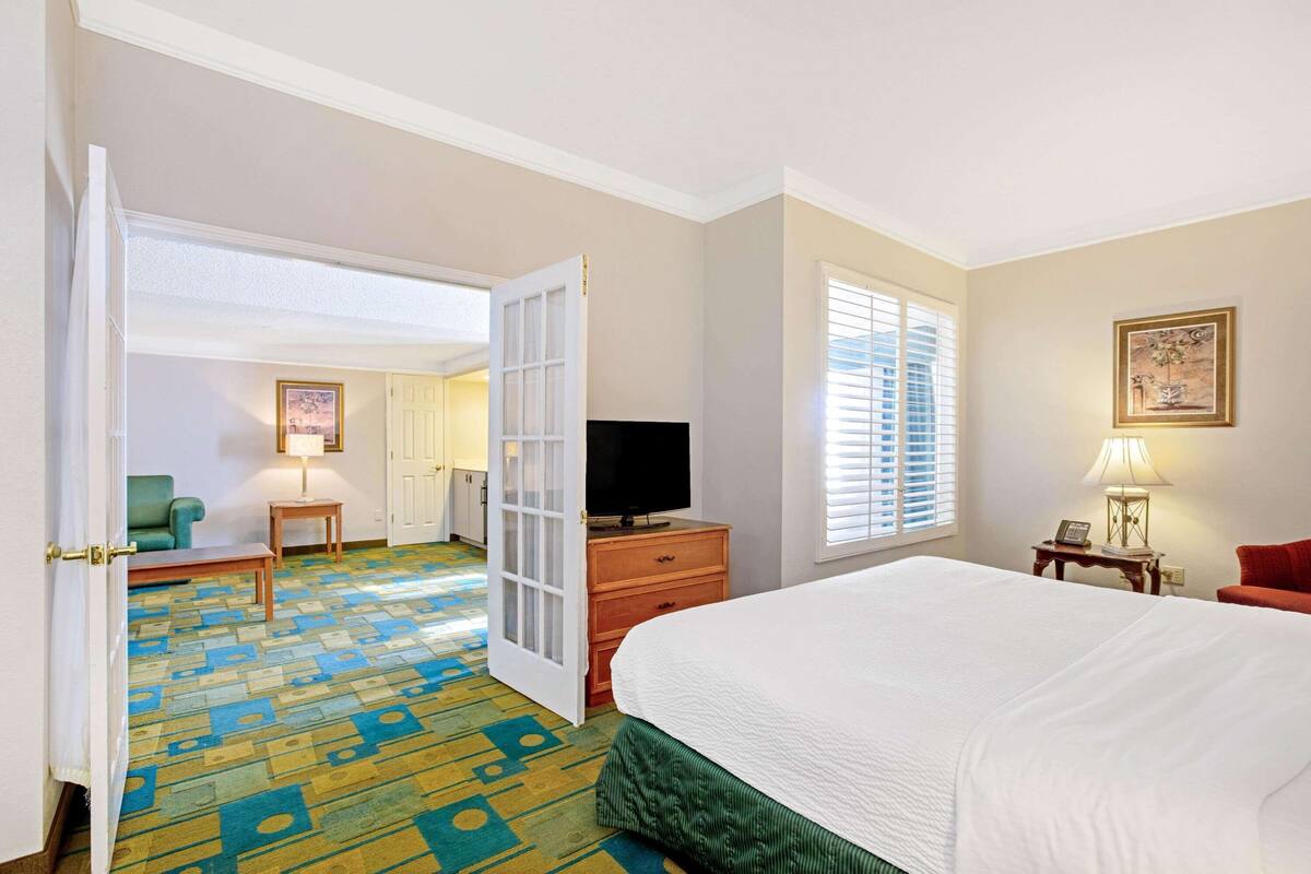 A hotel room with a bed, a television on a wooden dresser, a chair, and a lamp.