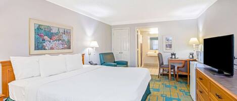 Quarto de hotel com uma cama grande, uma escrivaninha com cadeira, televisão e um quadro na parede.