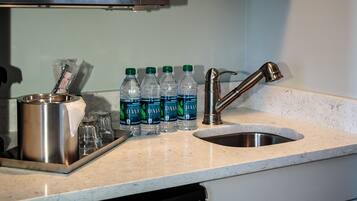 Una encimera de cocina con un lavamanos de acero inoxidable, un grifo y una bandeja con botellas de agua y vasos.