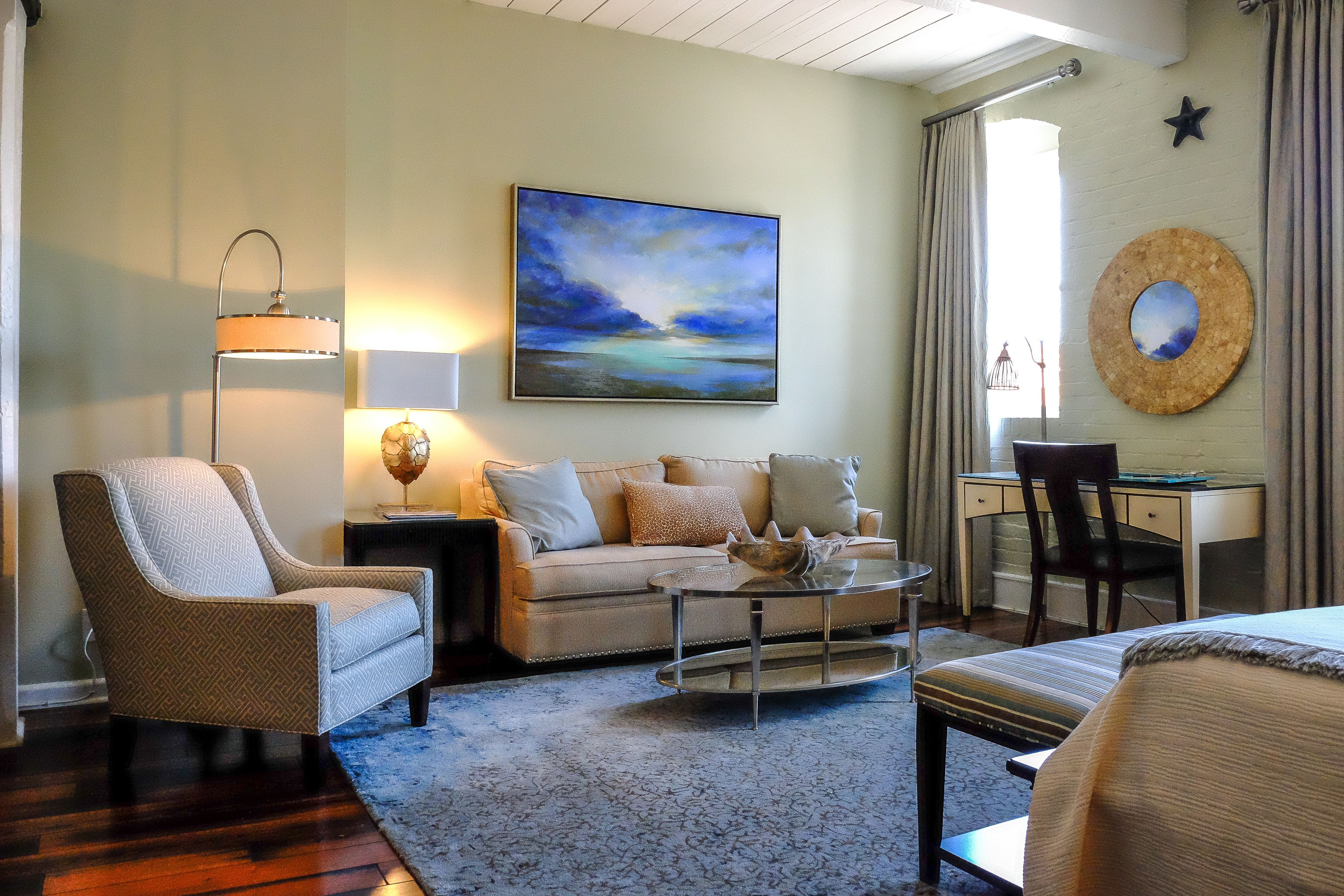 A cozy living room with a sofa, armchair, coffee table, and a painting on the wall.