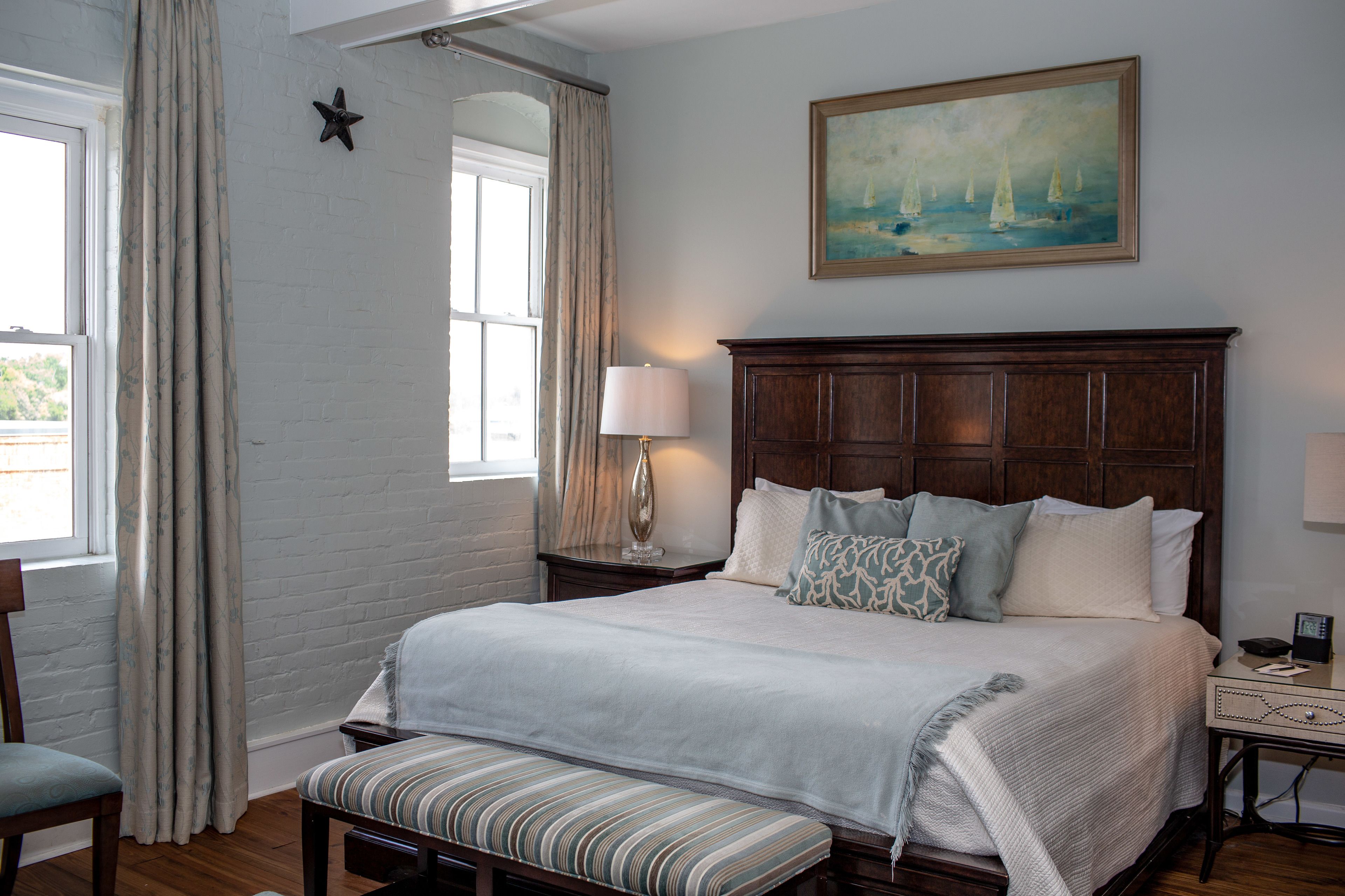 Une chambre à coucher bien rangée, avec un grand lit, un banc, une table de chevet, une lampe et un tableau au mur.