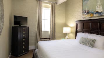 A hotel room with a bed, a television on a cabinet, a painting on the wall, and a window with curtains.