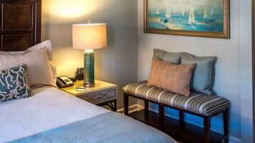 A hotel room with a bed, bedside lamp, a bench with cushions, a painting of sailboats, and a telephone on the nightstand.