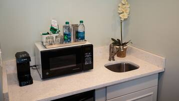 A kitchen counter with a microwave, coffee maker, and water bottles.