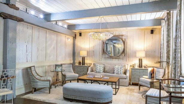 A spacious living room with a wooden floor, a round mirror, a sofa, two armchairs, a coffee table, and a side table with lamps. - Olde Harbour Inn (Savannah)