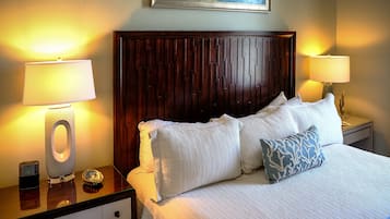 A neatly made bed with white and blue patterned pillows, a wooden headboard, and two bedside lamps on a nightstand with a clock.
