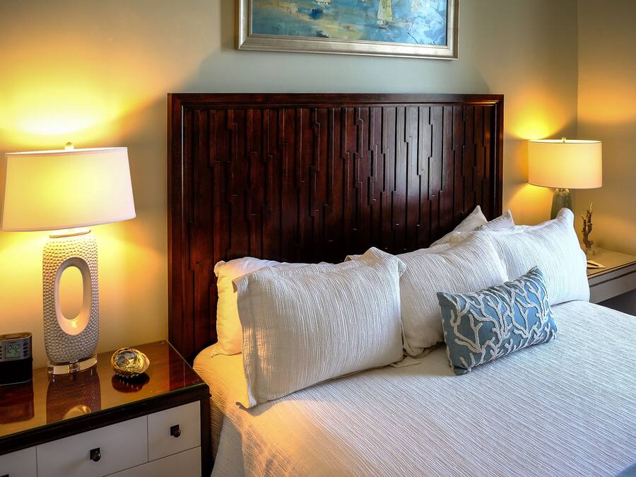 A neatly made bed with white and blue patterned pillows, a wooden headboard, and two bedside lamps on a nightstand with a clock.
