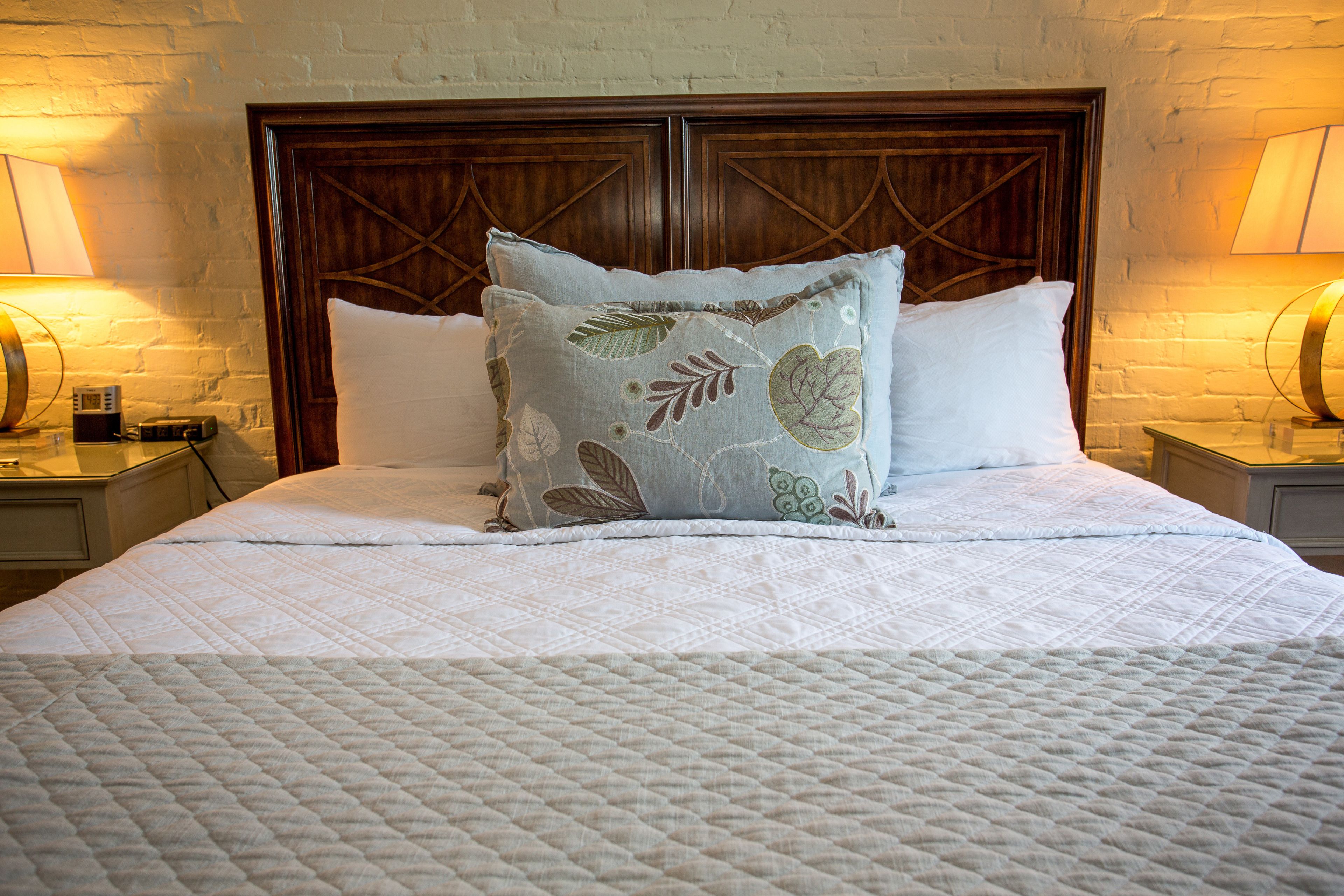 A neatly made bed with a quilted white bedspread, a decorative pillow with leaf patterns, and a wooden headboard.