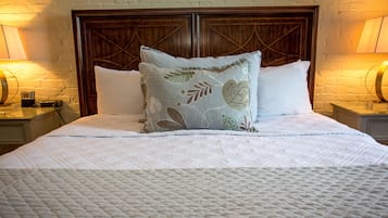 Una cama bien hecha con una colcha blanca acolchada, un cojín decorativo con motivos de hojas y un cabecero de madera.