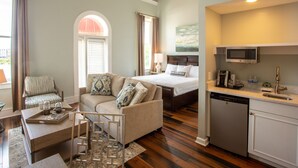A hotel room with a bed, a sofa, a dining table, and a kitchen area with a microwave and dishwasher. - Olde Harbour Inn (Savannah)
