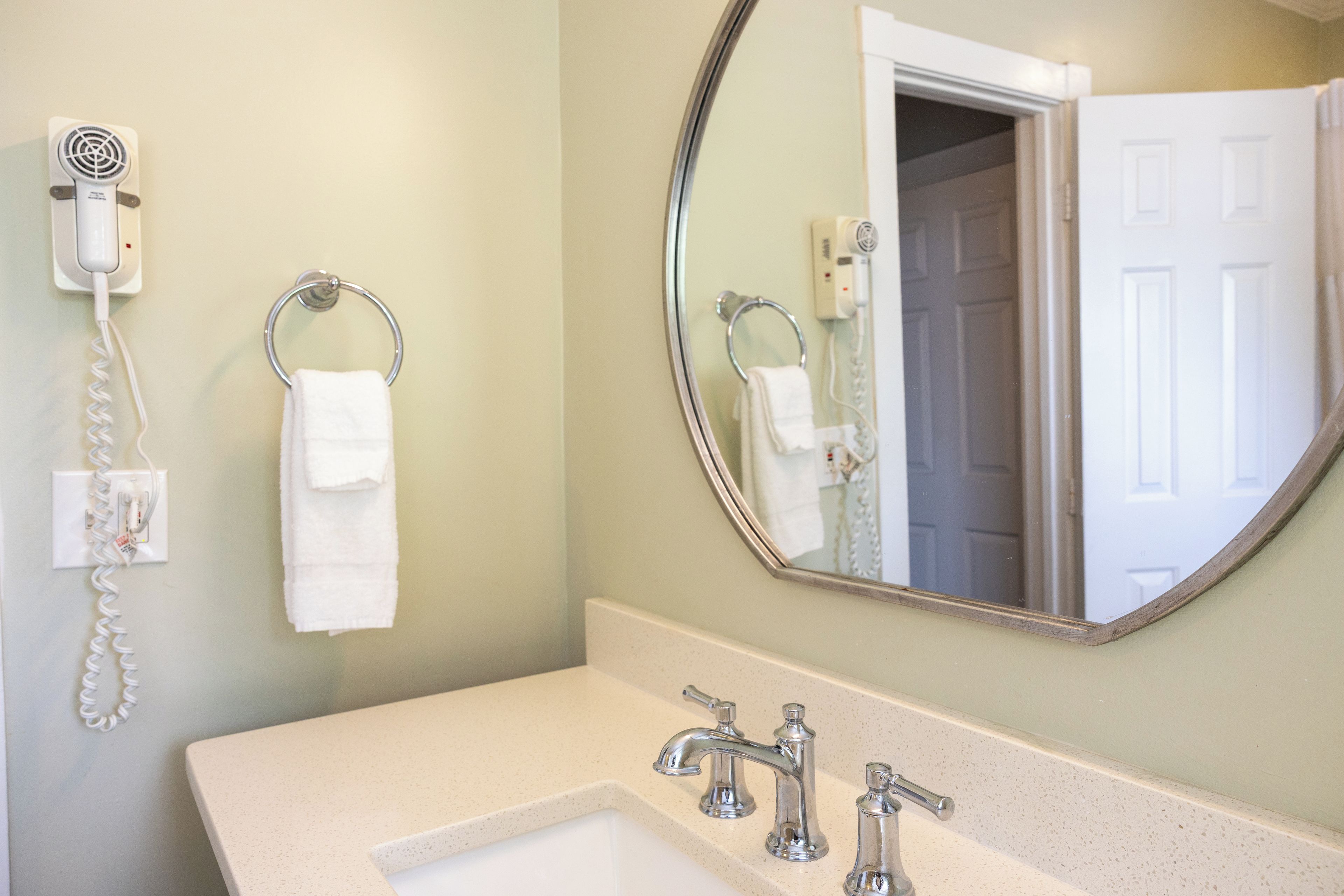 A bathroom with a sink, two faucets, a mirror, and a hairdryer on a wall-mounted outlet.