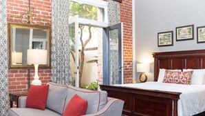 A hotel room with a bed, a sofa, a mirror, and a window with a view of trees. - East Bay Inn, Historic Inns of Savannah Collection (Savannah)