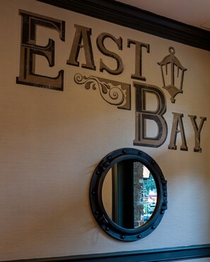 A wall with the words "EAST BAY" in large letters, a decorative lantern, and a round mirror.