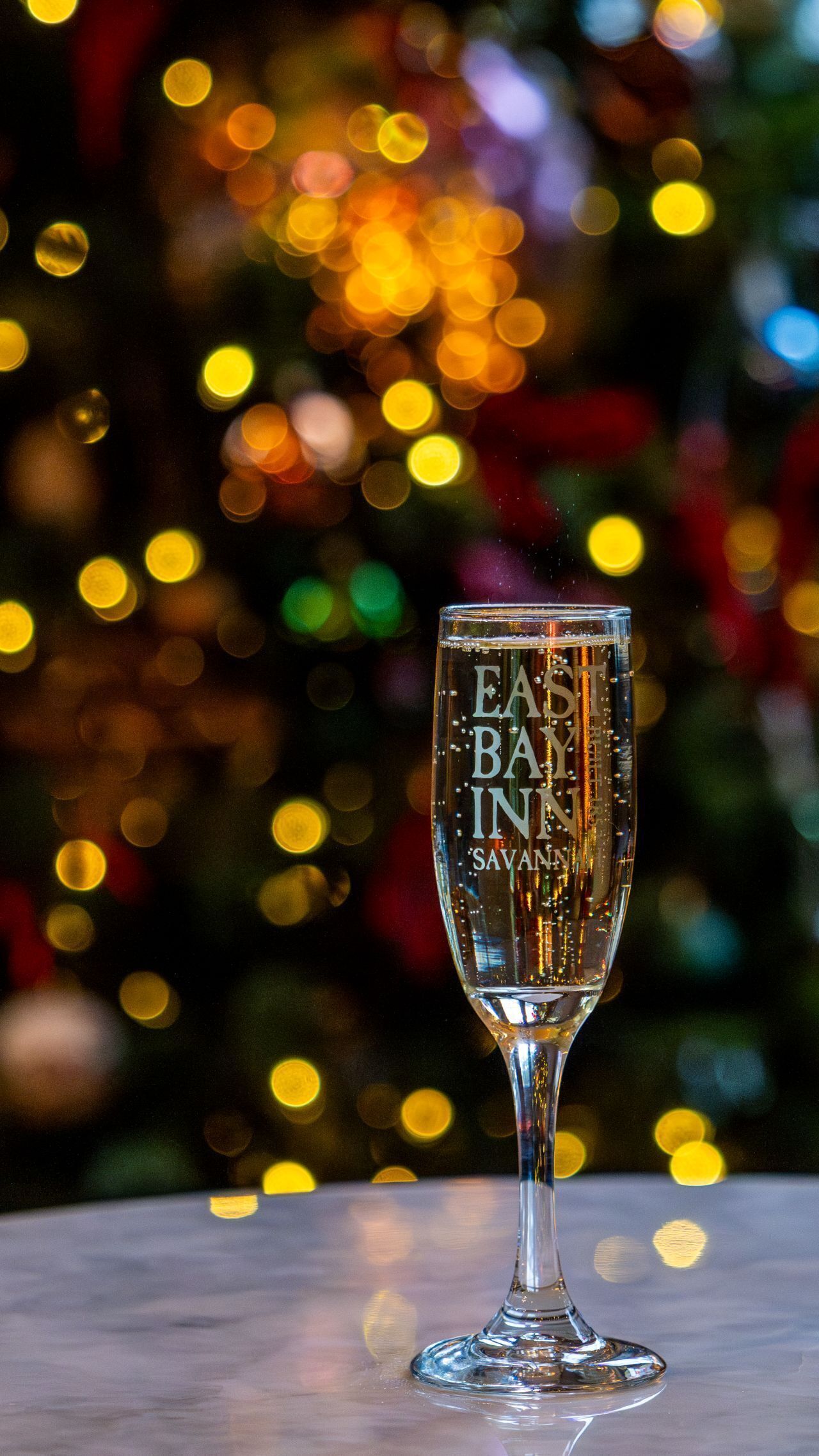 A clear glass with "EAST BAY INN SAVANNAH" text, set against a blurred background of colorful lights.