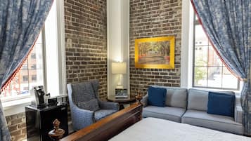 A hotel room with a brick wall, a bed, a sofa, a chair, a lamp, and a painting.