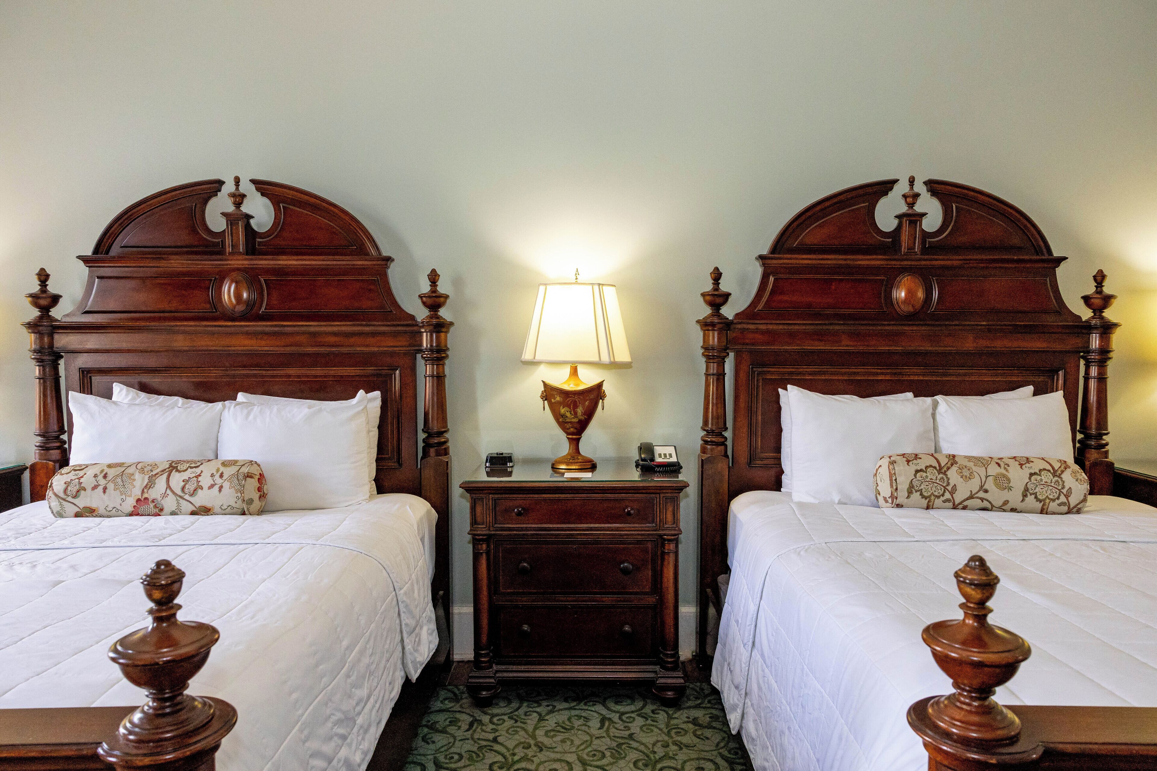 A double room with two wooden beds, a nightstand with a lamp, and a patterned rug.