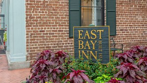 A sign for East Bay Inn, a brick building with green shutters, and a flower bed with purple foliage. - East Bay Inn, Historic Inns of Savannah Collection (Savannah)