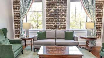 A living room with a brick wall, a gray sofa, green armchairs, and a glass coffee table.