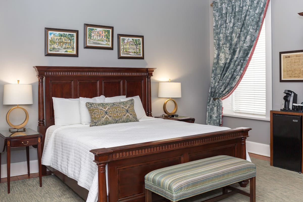 A neatly made bed with a wooden headboard, two bedside tables with lamps, a bench at the foot of the bed, and three framed pictures on the wall.