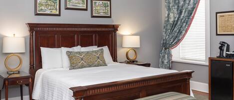 Una cama bien hecha con cabecera de madera, dos mesitas de noche con lámparas, un banco al pie de la cama y tres cuadros enmarcados en la pared.