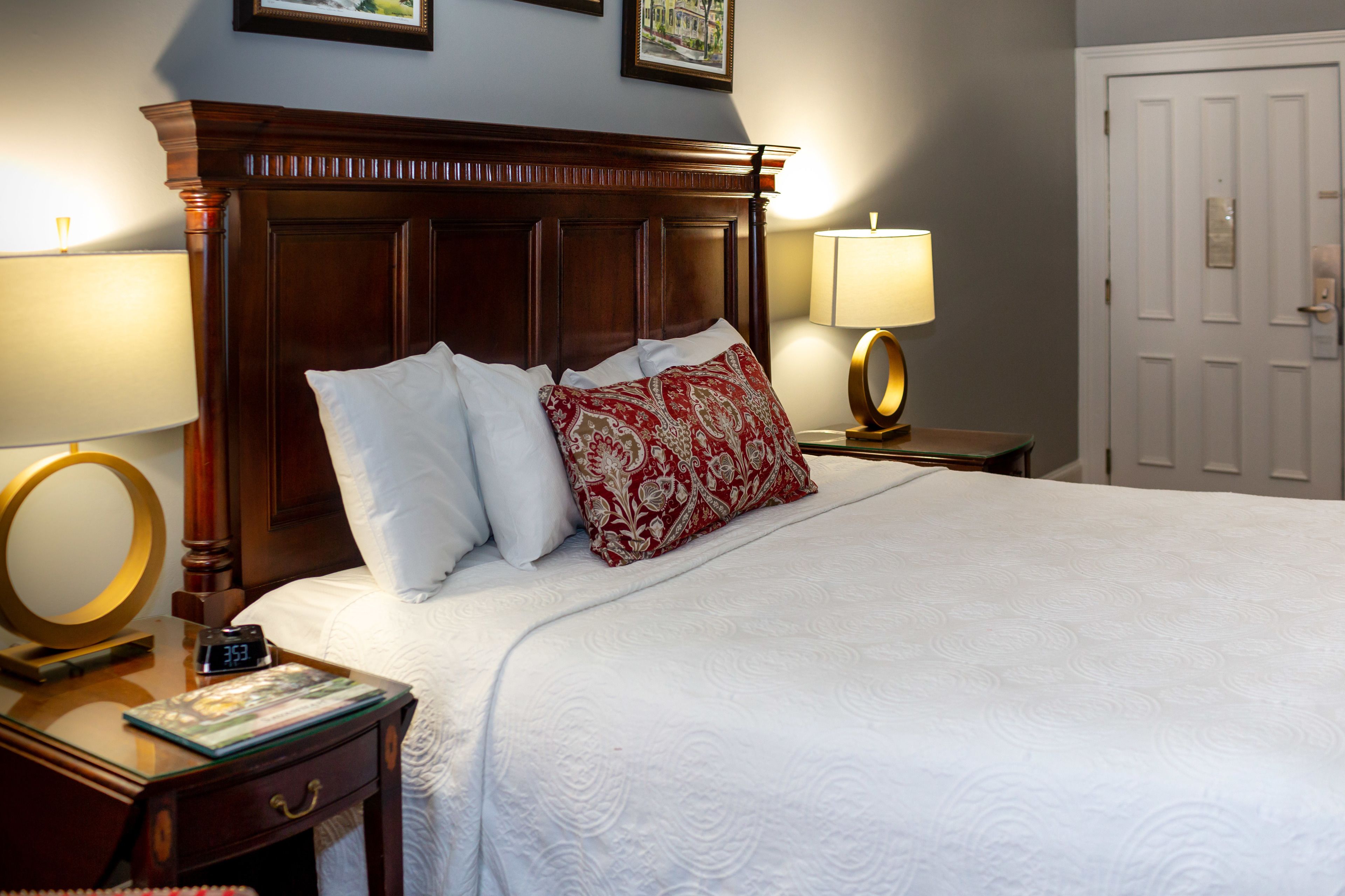 A neatly made bed with white and red pillows, a wooden headboard, and two bedside lamps.