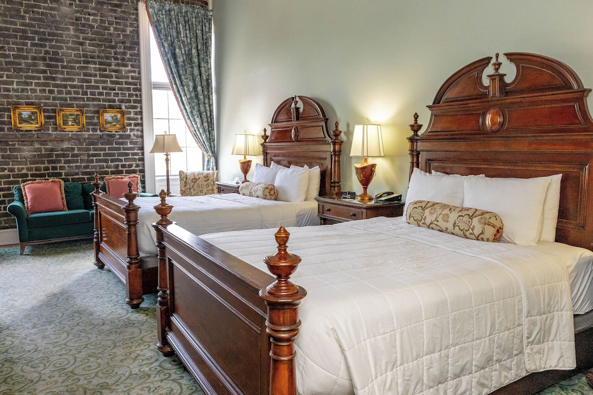 A hotel room with two wooden beds, a green sofa, and a brick wall.