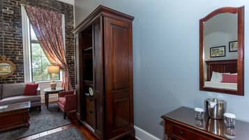 A room with a brick wall, a wooden wardrobe, a mirror, a sofa, a small table, and a lamp.