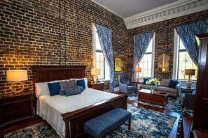 A hotel room with a brick wall, a large bed, a sitting area with a sofa and armchairs, and a dining table.