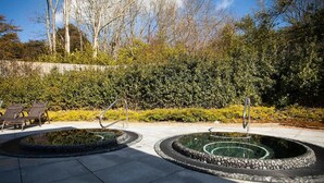 Una fuente circular con borde de piedra, rodeada por una zona pavimentada con sillas de descanso.