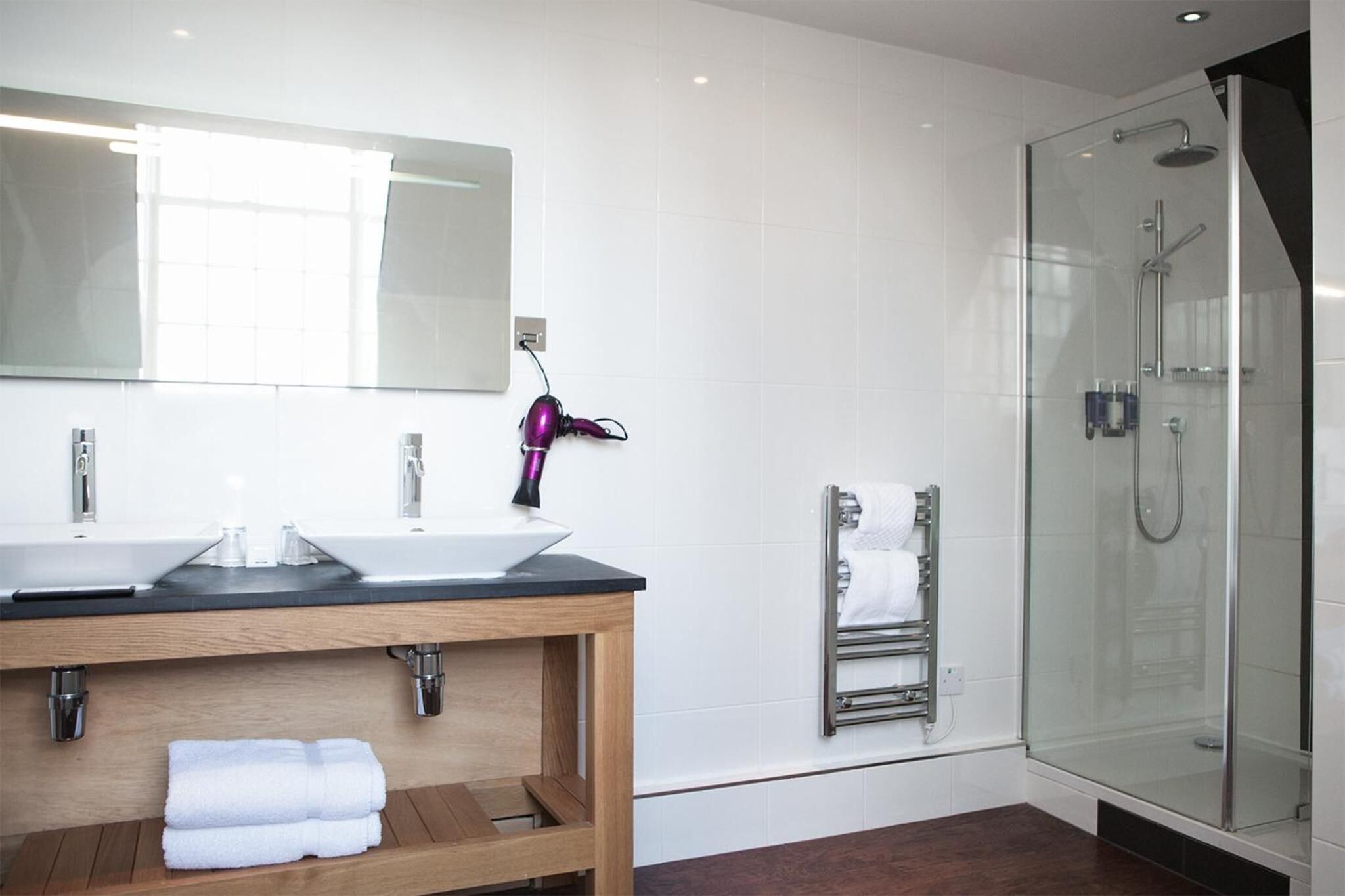 Een moderne badkamer met twee wastafels, een grote spiegel, een douchecabine van glas en een handdoekrek.