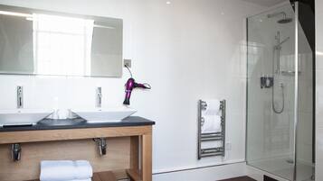 A modern bathroom with two sinks, a large mirror, a glass shower enclosure, and a towel rack.