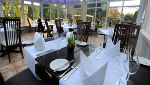 Un invernadero con mesas dispuestas para comer, con manteles blancos, cubiertos ordenados y plantas en macetas.